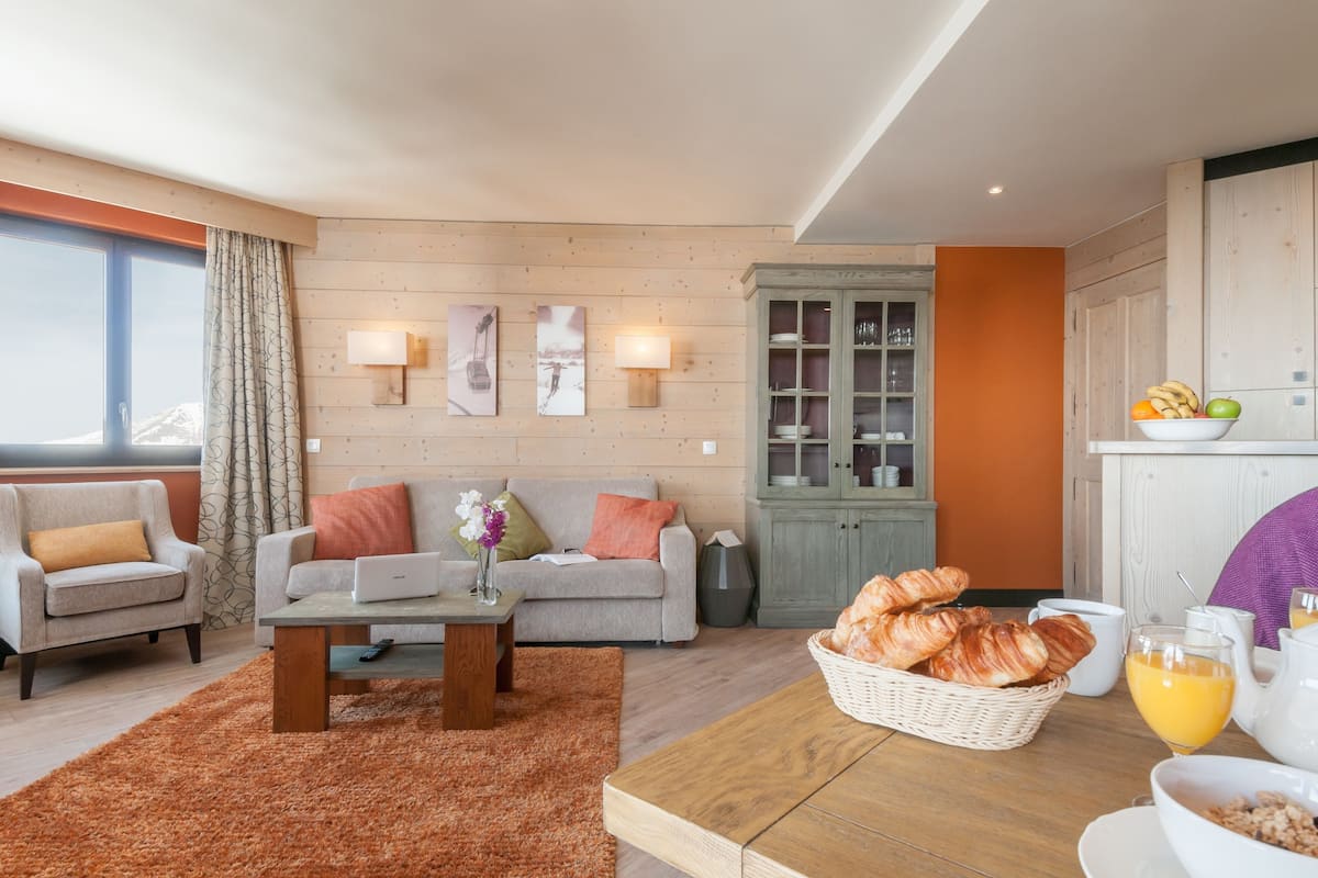 A living room with a sofa, two armchairs, a coffee table, and a dining table with breakfast items.