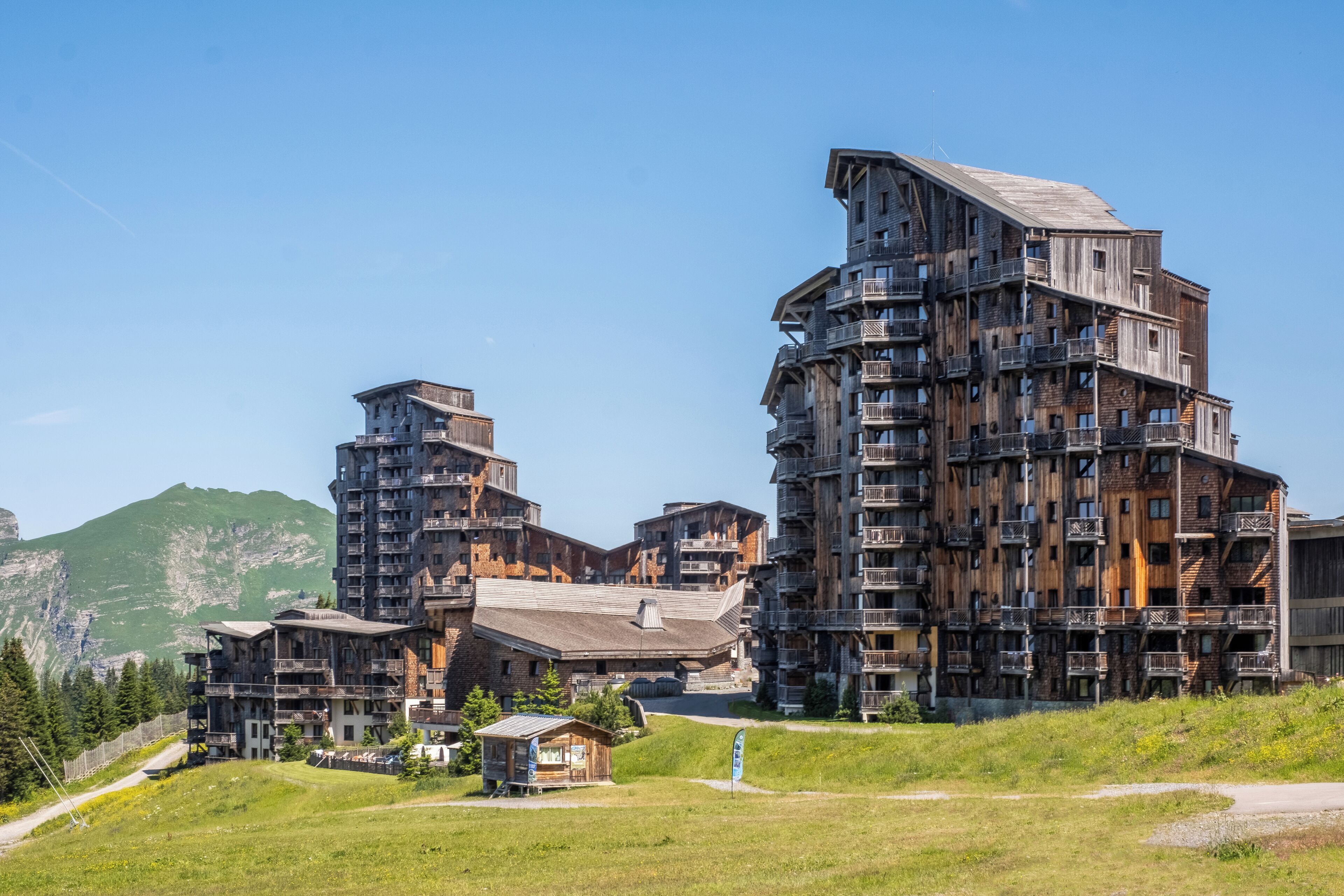 A multi-story hotel with a rustic wooden facade, balconies, and a mountainous backdrop.