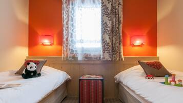A hotel room with two beds, a window with patterned curtains, wall-mounted lamps, and a small table with a red box.