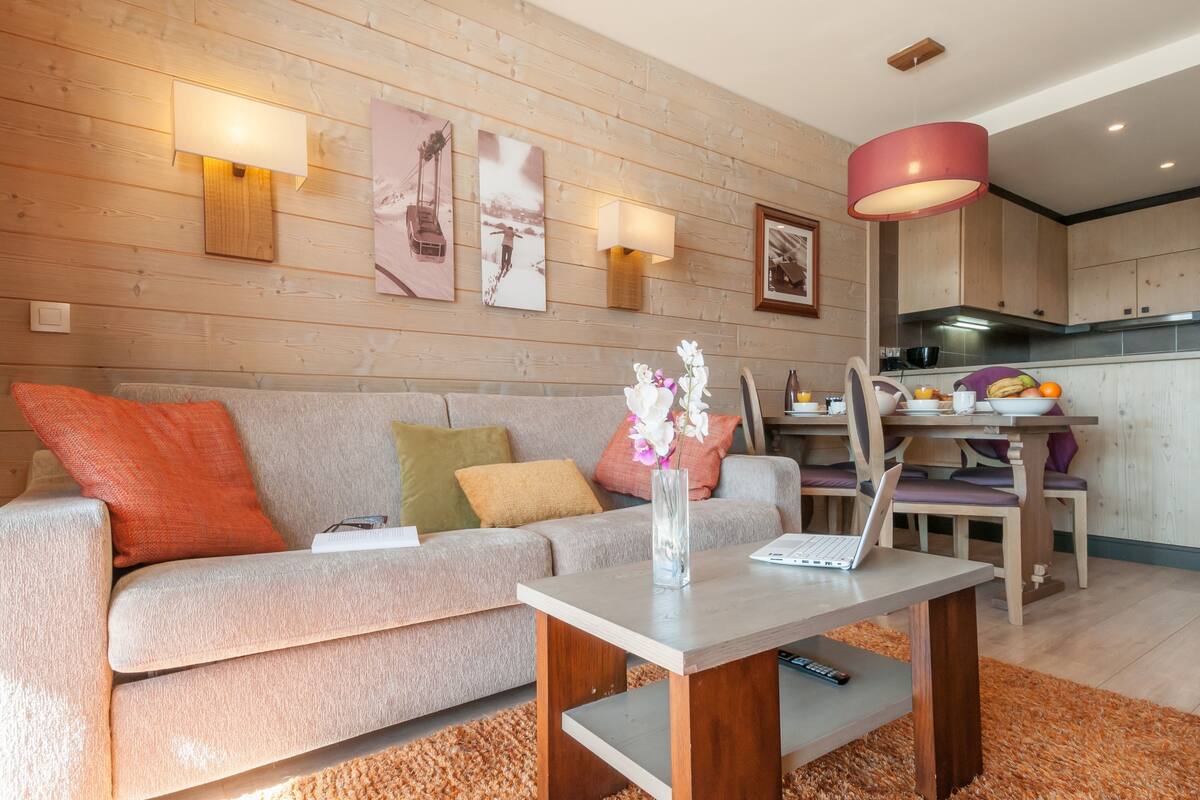 A modern living room with a grey sofa, a wooden coffee table, and a dining area with a wooden table and chairs.
