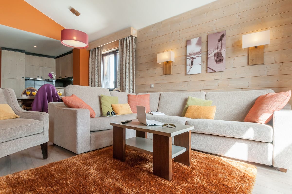 A modern living room with a sofa, armchairs, a coffee table, and a kitchen in the background.