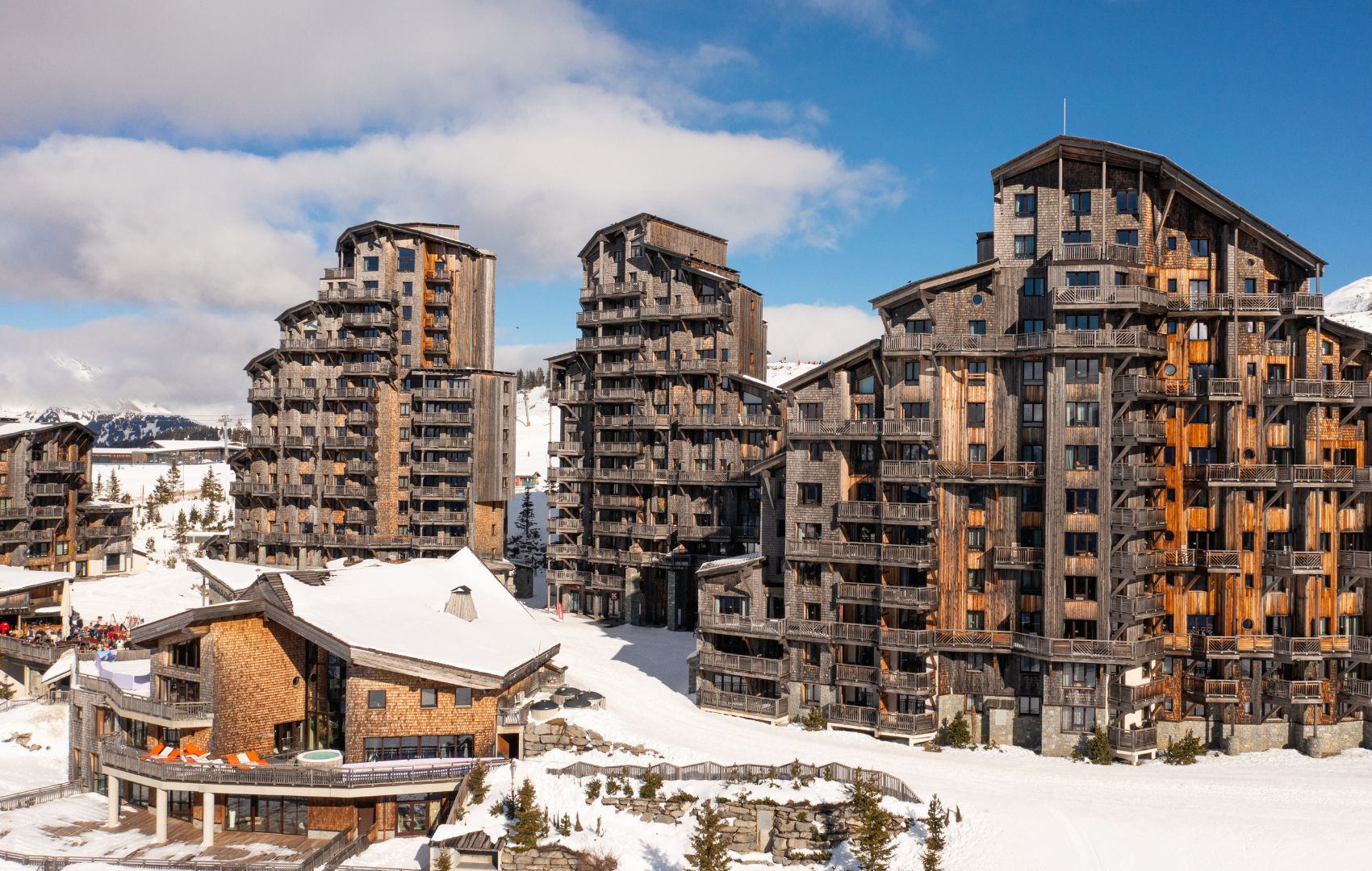 Une station de ski moderne avec des bâtiments à plusieurs étages dotés de balcons et de façades en bois.