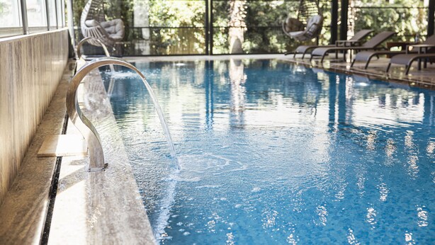Une piscine intérieure à l’eau claire, dotée de chaises longues et offrant une vue sur la verdure environnante.