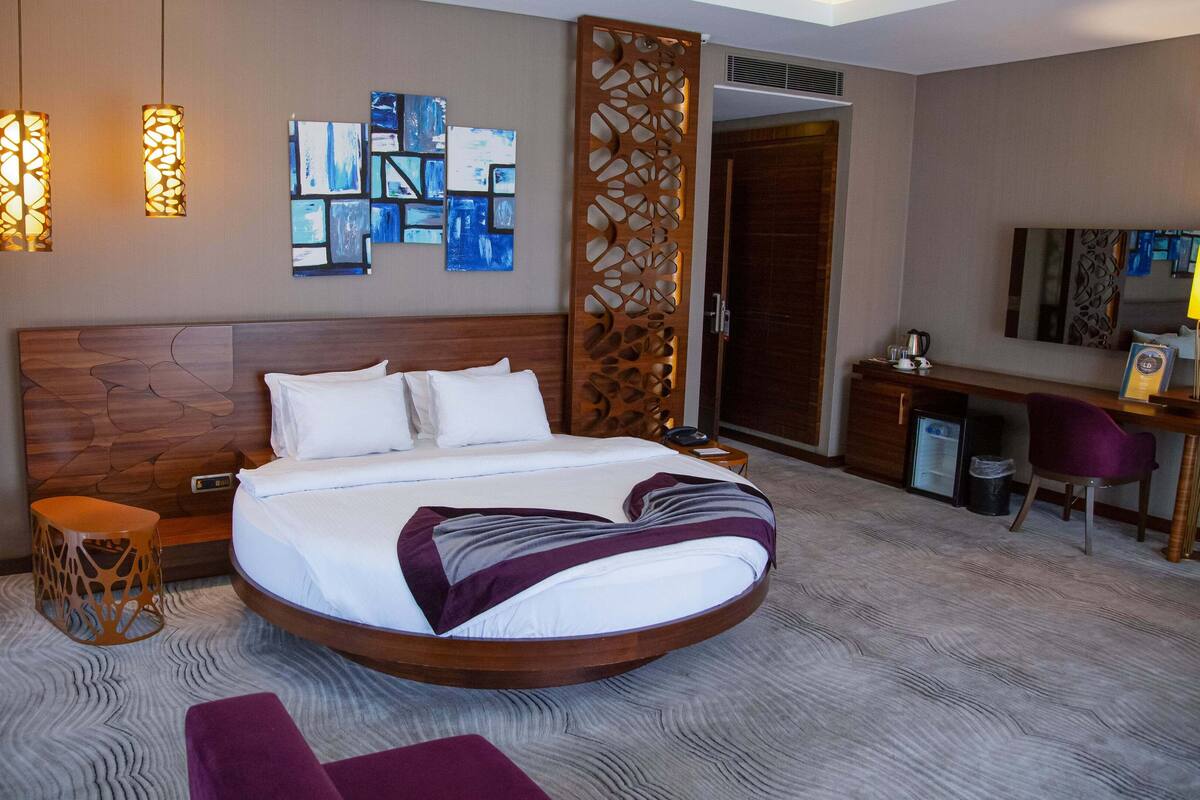 Habitación de hotel con cama redonda, escritorio, silla y pared decorativa con arte abstracto.