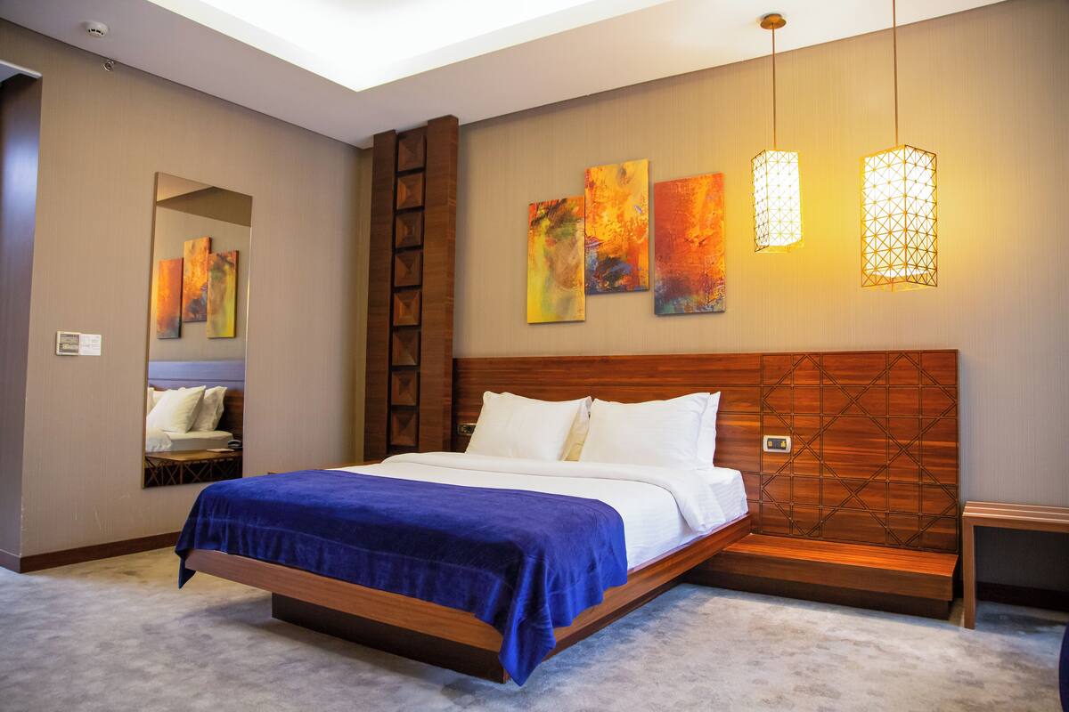 Una habitación de hotel moderna con una cama grande, un cabecero de madera y una obra de arte en la pared.