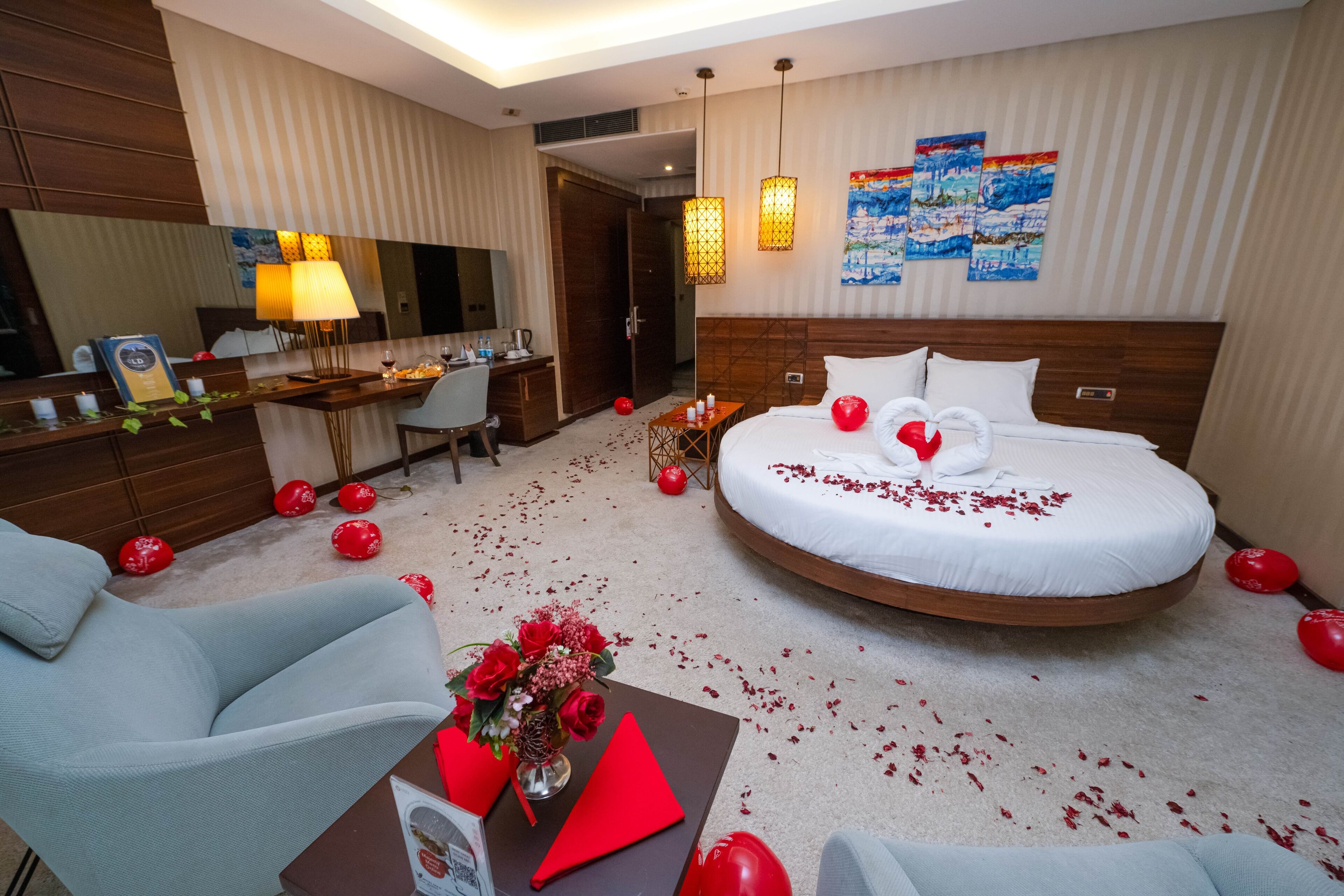 A hotel room with a round bed, a desk, a chair, and a large mirror.