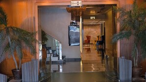 Un hall d’hôtel avec une entrée en verre, des palmiers et un escalier menant à l’étage supérieur.