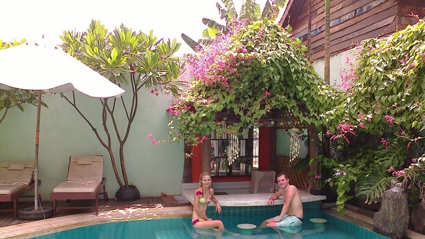 A swimming pool with two lounge chairs and a bench, surrounded by lush greenery and flowering plants. - Siem Reap Riverside Hotel (Siem Reap)
