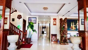 A hallway with a wooden staircase, a large potted plant, and a statue. - Siem Reap Riverside Hotel (Siem Reap)