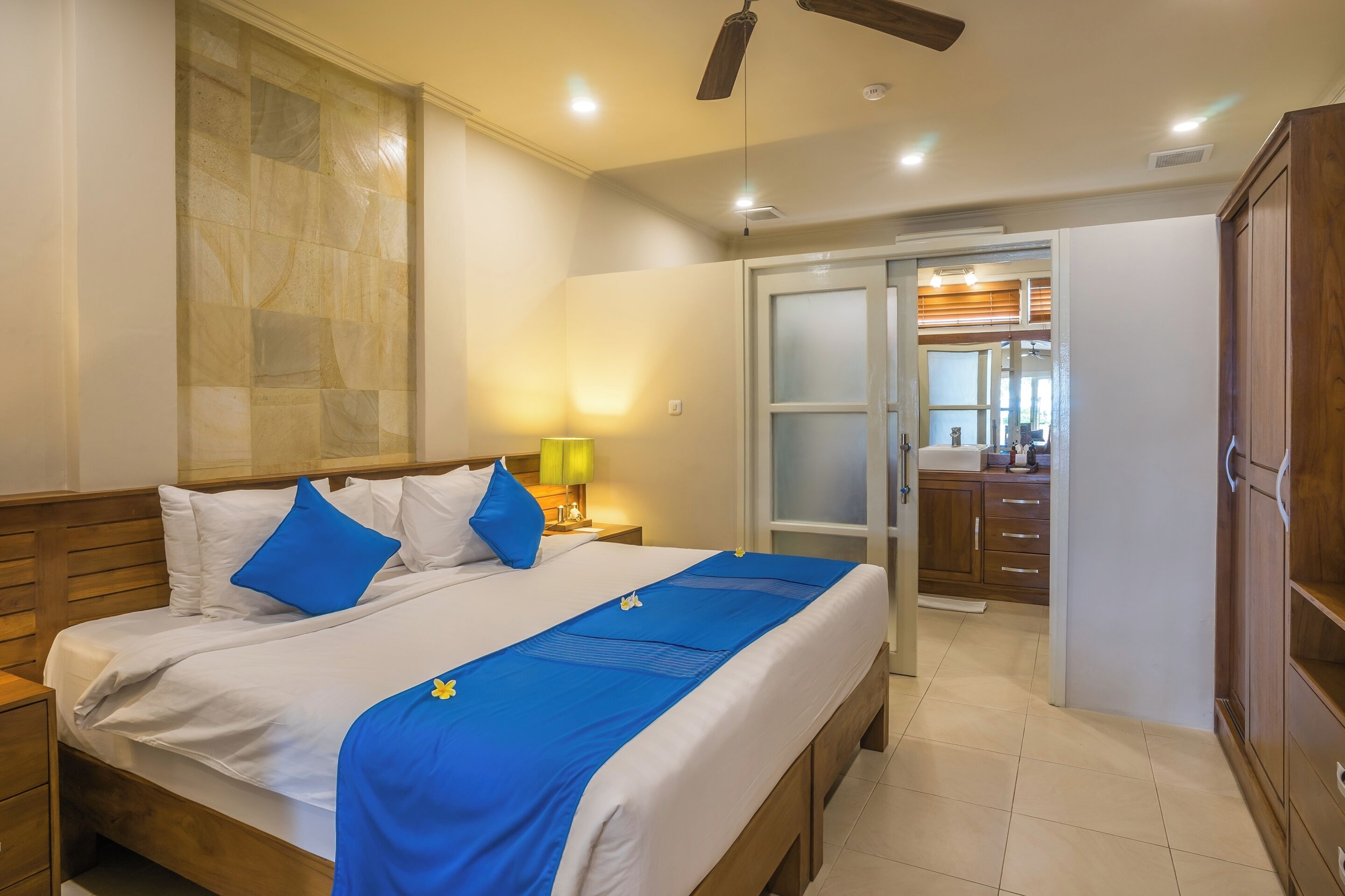 A hotel room with a bed, a nightstand, a lamp, a wardrobe, and a sliding door to the bathroom.