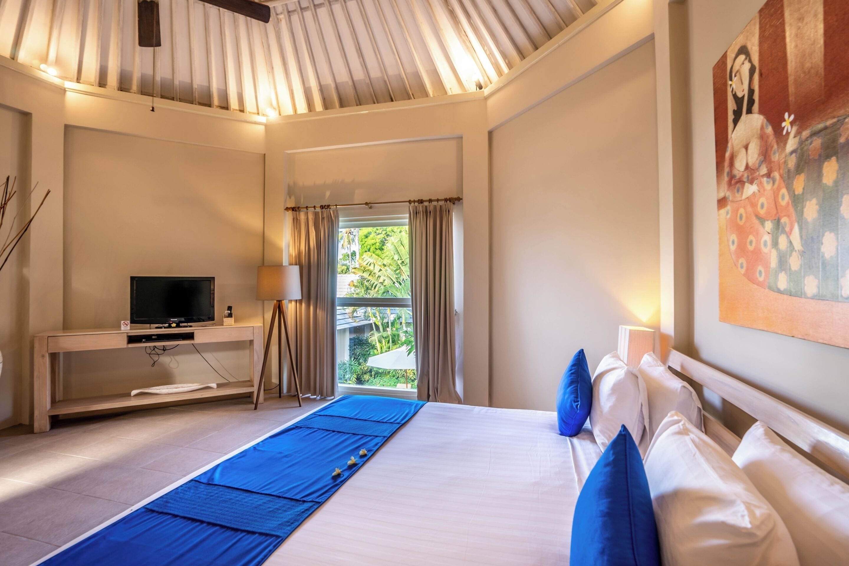 Een hotelkamer met een bed, een televisie op een standaard, een balkon met gordijnen en een schilderij aan de muur.