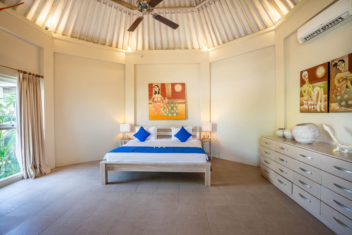 Ein Schlafzimmer mit einem Bett, Nachttischlampen, einem Deckenventilator, einem Gemälde und einer Kommode.