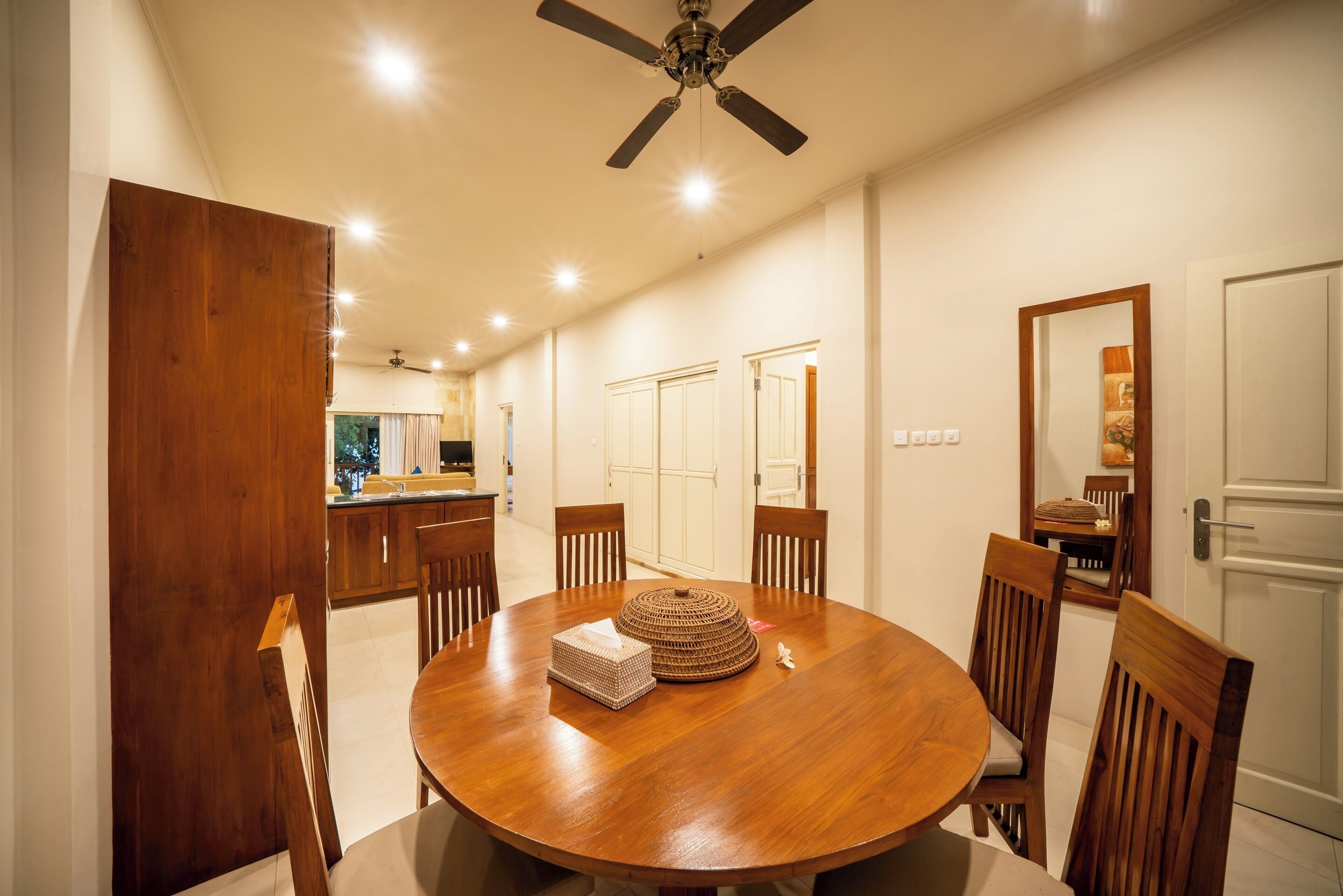 A dining area with a round wooden table, six wooden chairs, a ceiling fan, and recessed lighting.