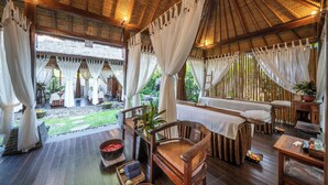 A wooden deck with a thatched roof, white curtains, and a dining area with tables and chairs. - The Lovina (Buleleng)