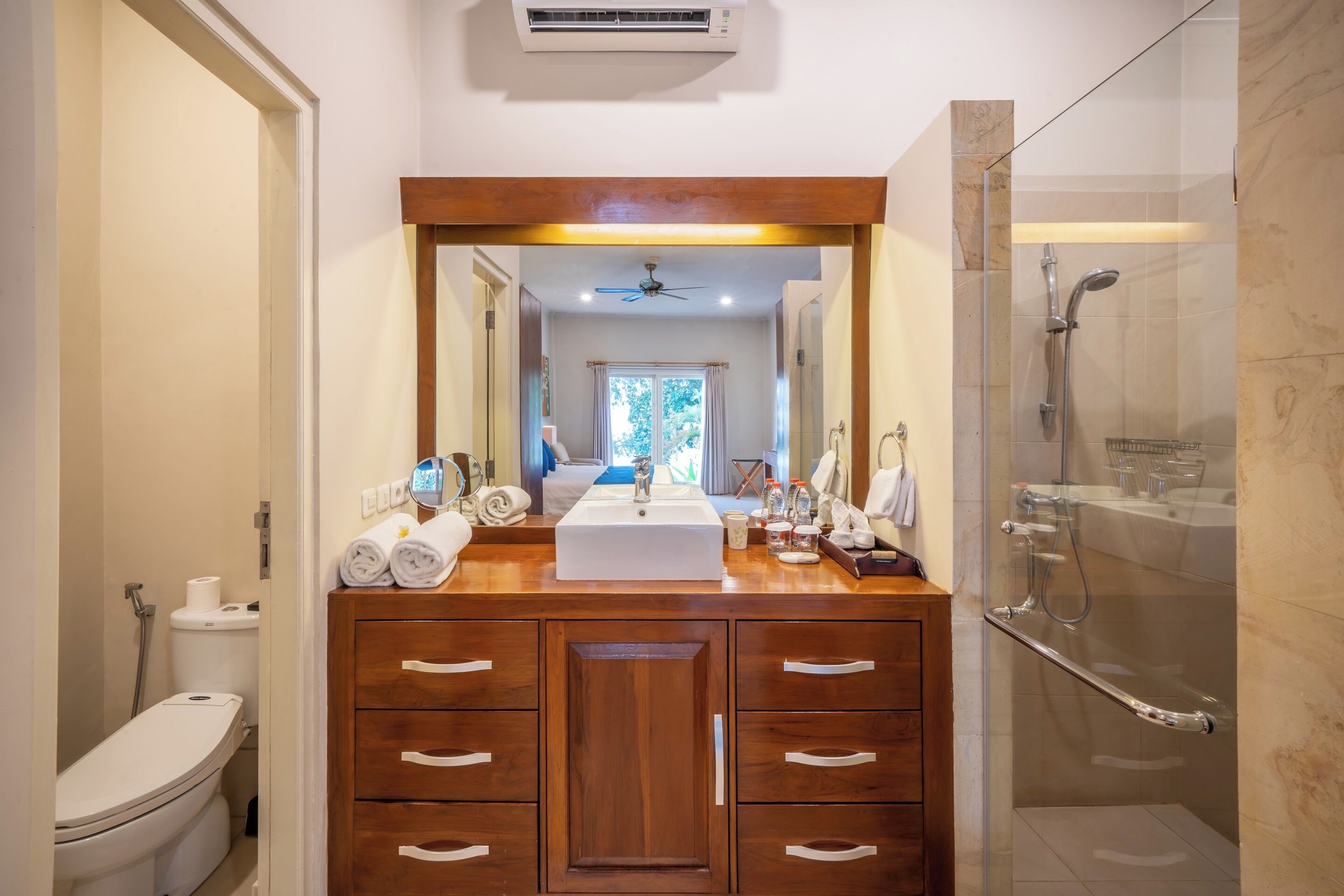 A bathroom with a wooden vanity, a large mirror, a shower, and a toilet.