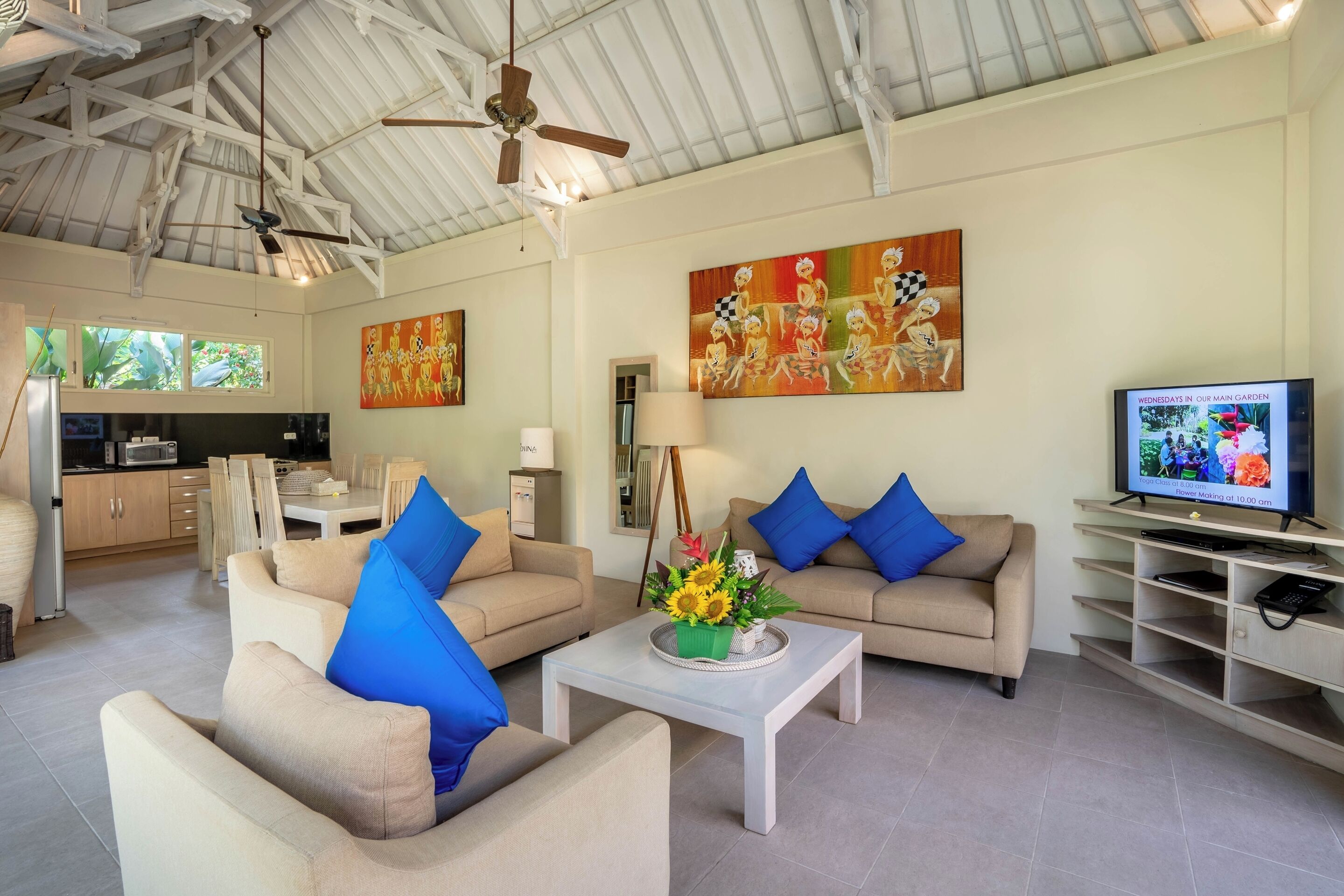 A spacious living room with beige sofas, a coffee table with a floral centerpiece, and a television on a wooden stand.