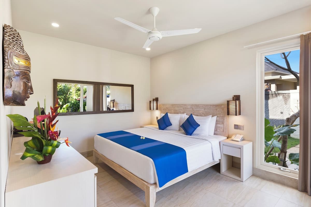 A bedroom with a bed, bedside tables, a ceiling fan, a nightstand, a mirror, and a window with a view.
