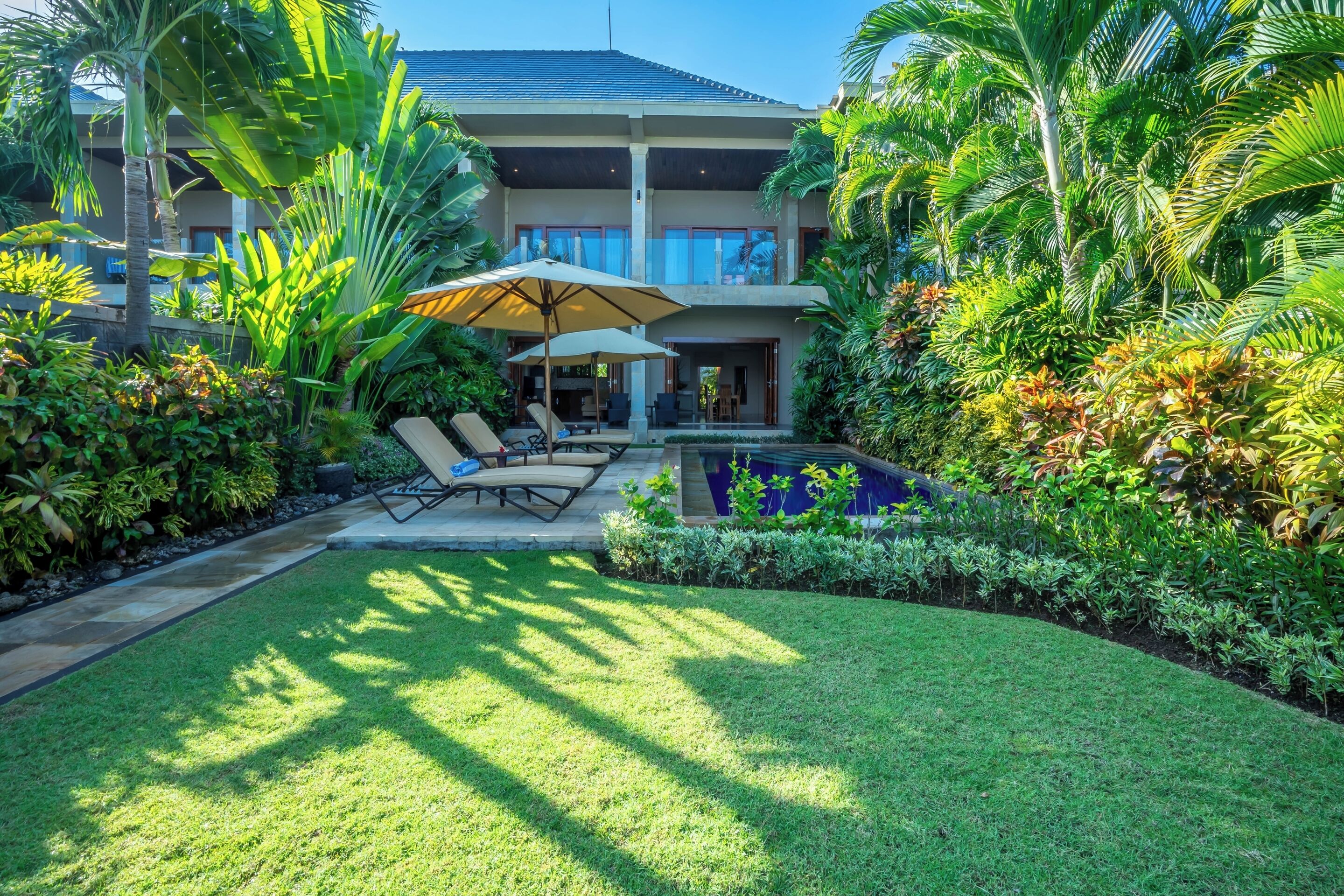 Una casa moderna con piscina, rodeada de exuberante vegetación tropical y un césped cuidado.