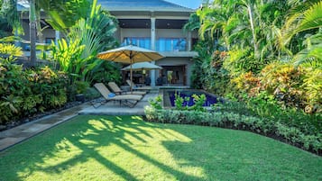 A modern house with a pool, surrounded by lush tropical plants and a well-maintained lawn.