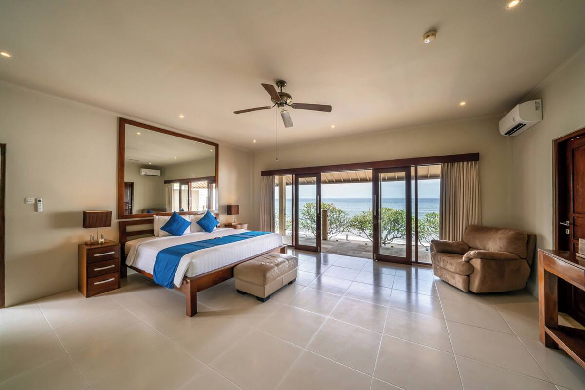Ein geräumiges Schlafzimmer mit einem großen Bett, einem Deckenventilator, Meerblick und einem Balkon.