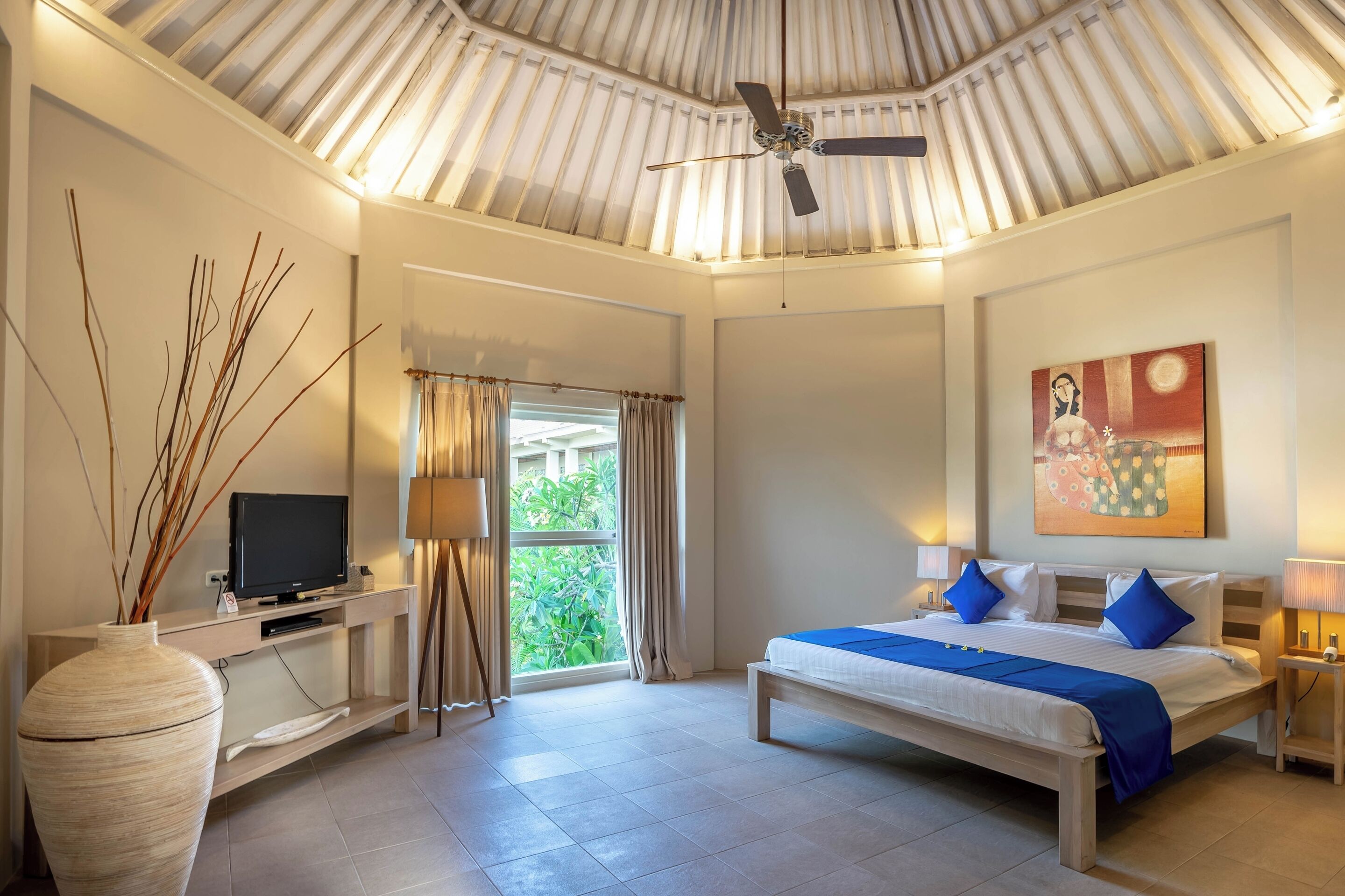 A bedroom with a bed, a television, a large vase, and a ceiling fan.