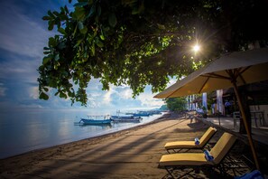 A beach with lounge chairs and umbrellas, boats in the water, and a clear sky. - The Lovina (Buleleng)