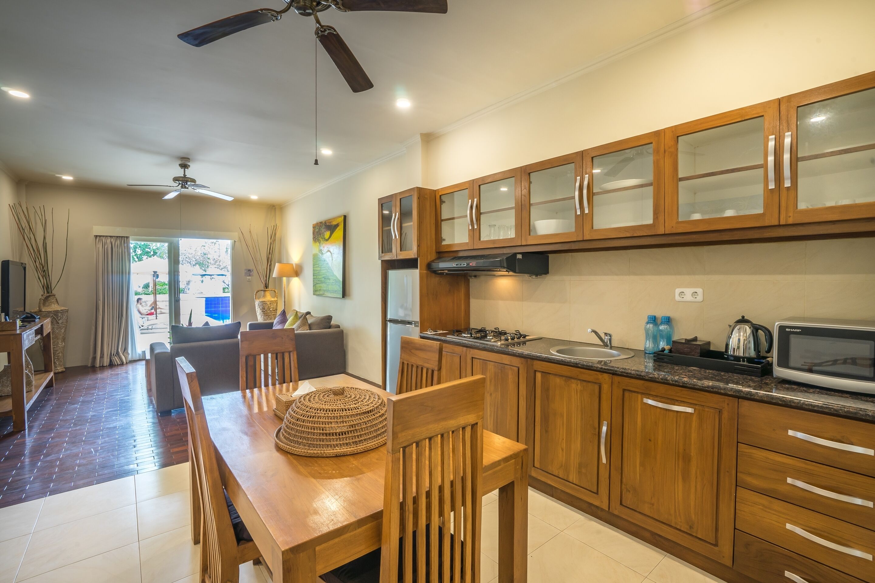 A modern kitchen with wooden cabinets, a dining area with a wooden table and chairs, and a ceiling fan.