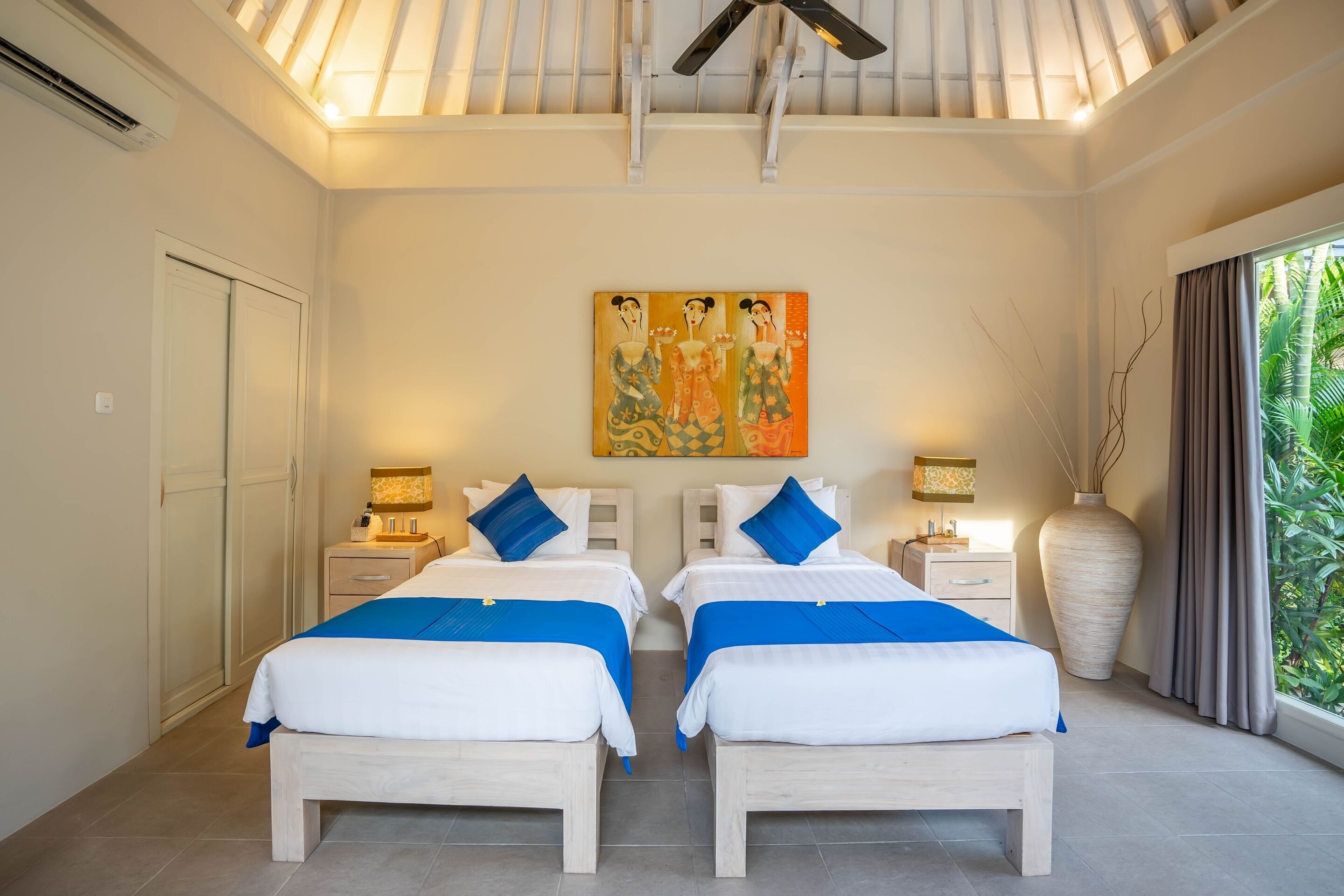 A double room with two beds, a ceiling fan, a large vase, and a painting on the wall.