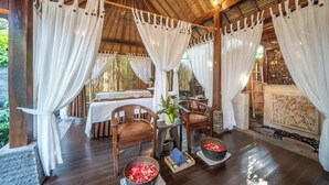 A spa area with wooden flooring, white curtains, and a seating area with chairs and tables. There are bowls of red flowers and a plant on the floor. - The Lovina (Buleleng)