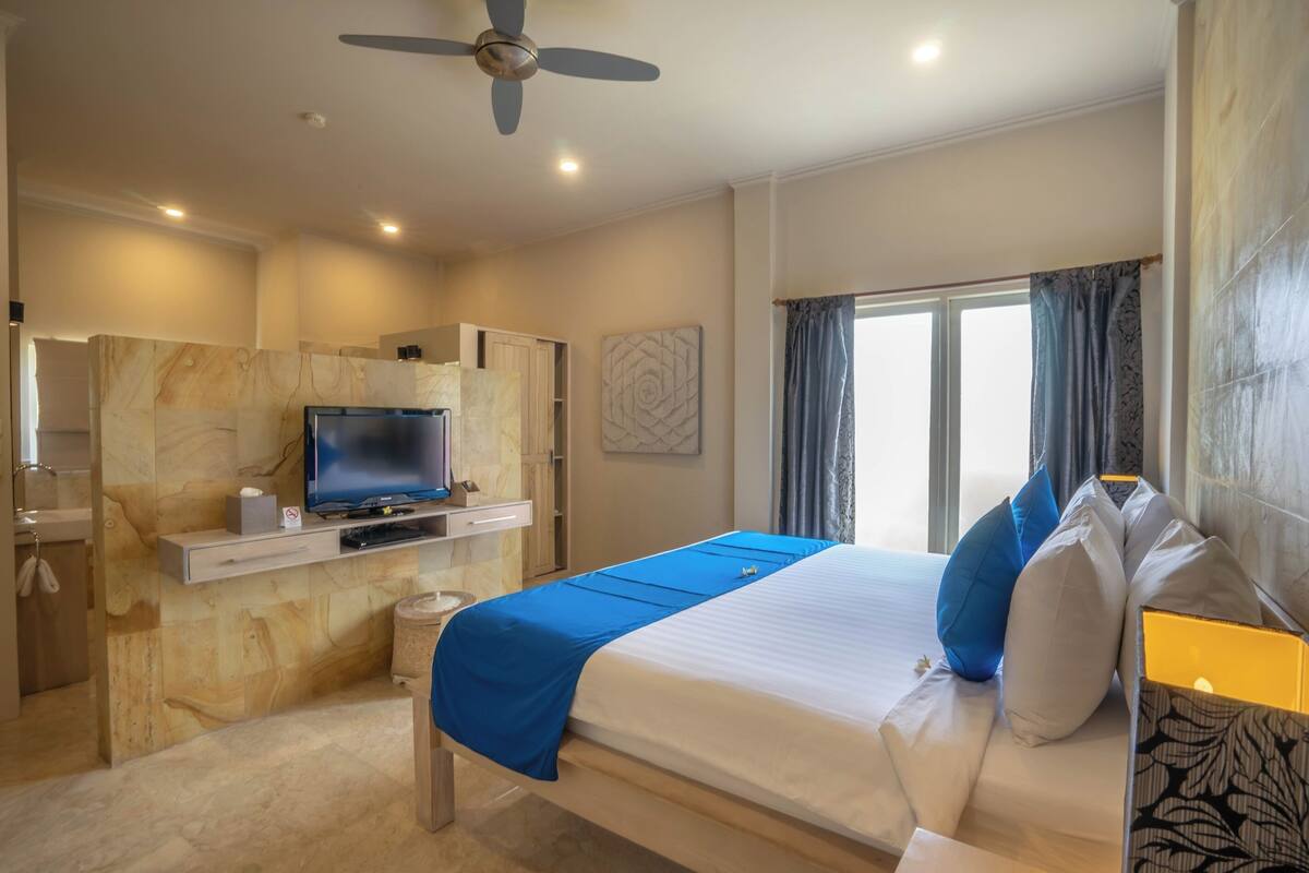 Ein Hotelzimmer mit Bett, Fernseher, Deckenventilator und einem Fenster mit Vorhängen.