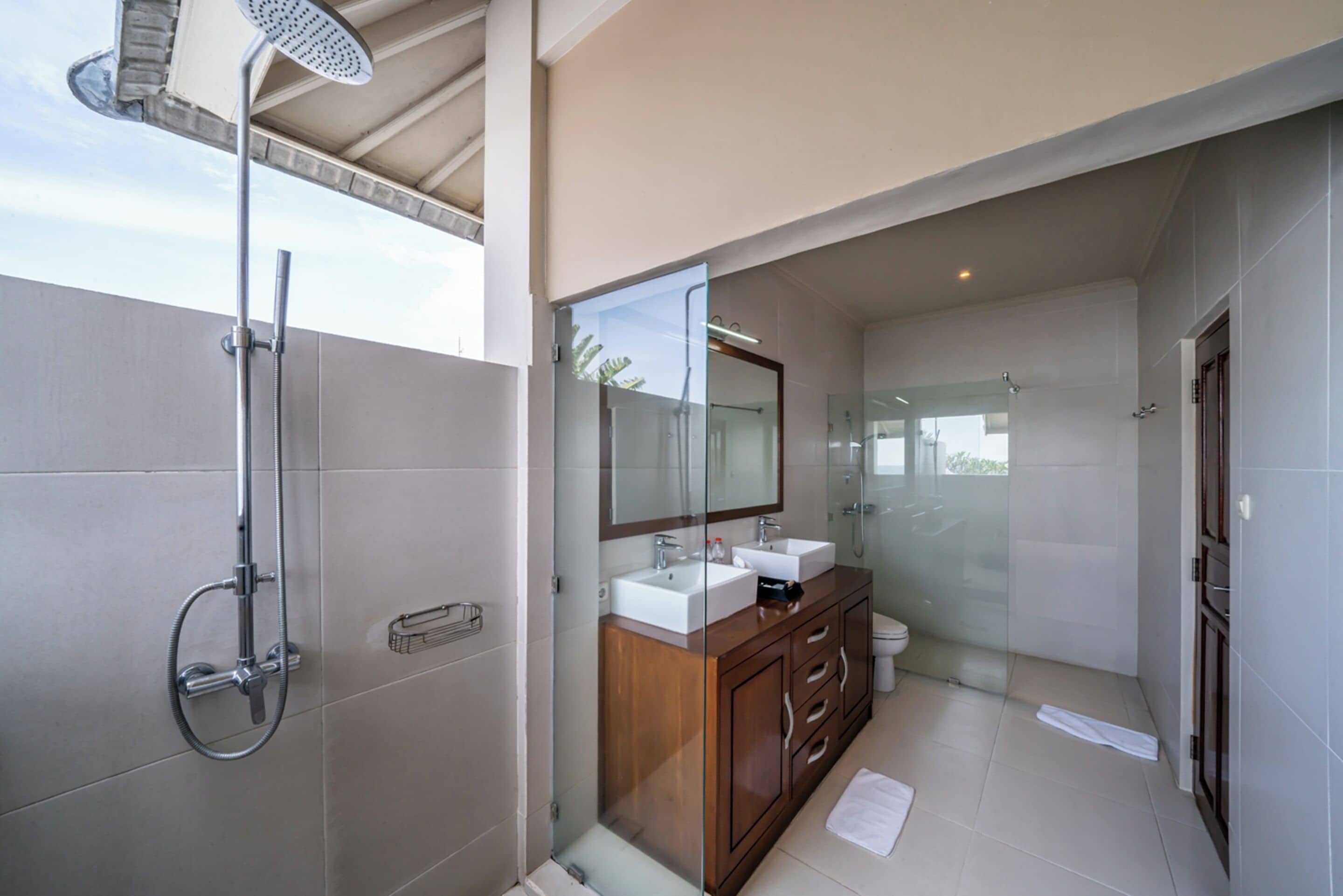 Une salle de bain moderne dotée d’une douche à parois de verre, d’un meuble-lavabo en bois avec un miroir et d’une grande fenêtre laissant entrer la lumière naturelle.