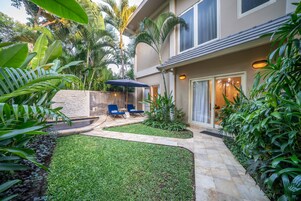 Un patio cuidado con césped, zona de estar y plantas tropicales.