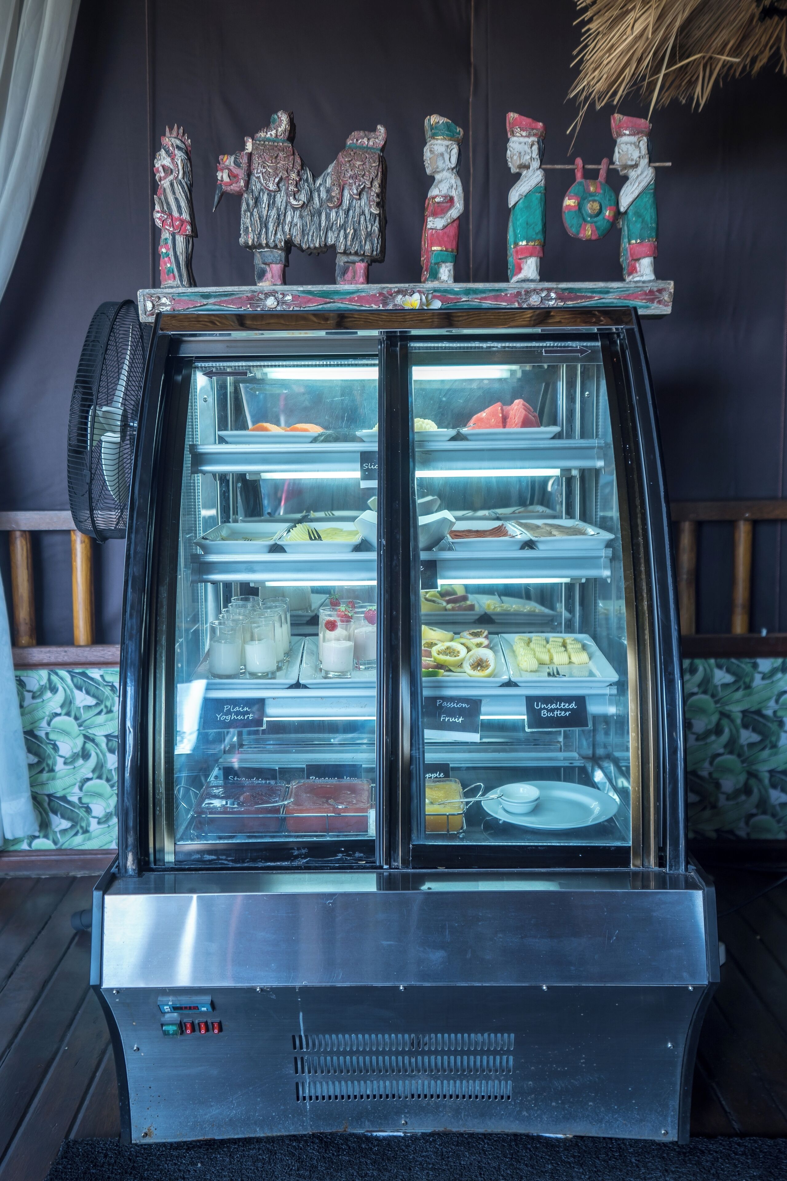A dessert display case with various sweets and a fan to the left.