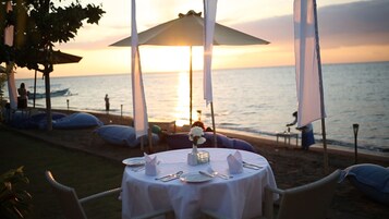 Un espacio de comedor al aire libre con mesas y sombrillas, con vista al mar al atardecer.