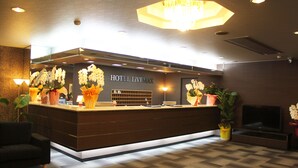 A hotel reception desk with a modern design, featuring a large chandelier, potted plants, and a television. - HOTEL LiVEMAX Iyo Mishima (Shikokuchuo)