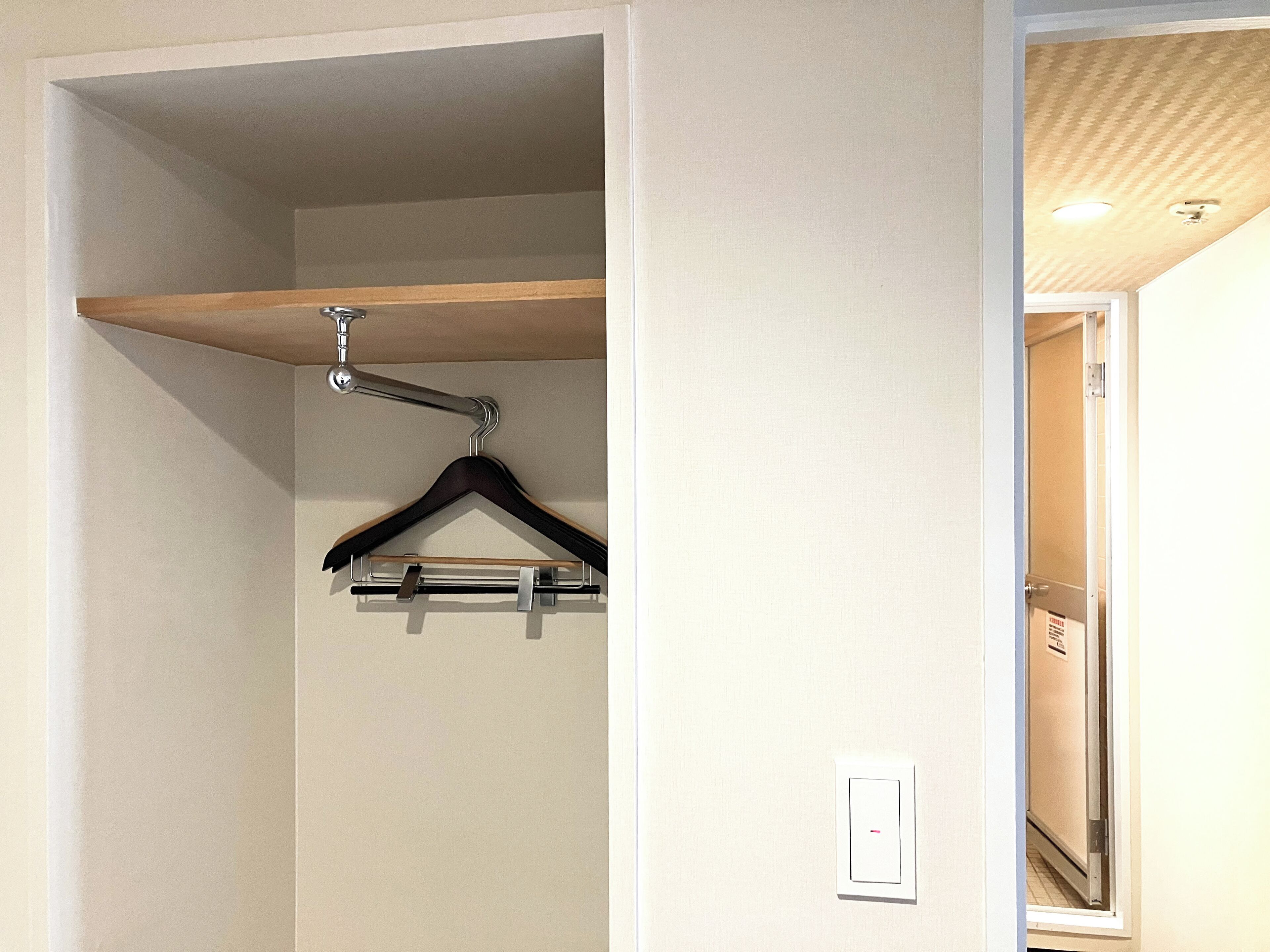 Ein Schrank mit einer Holzablage, einem Metallbügel und einem Lichtschalter an der Wand.