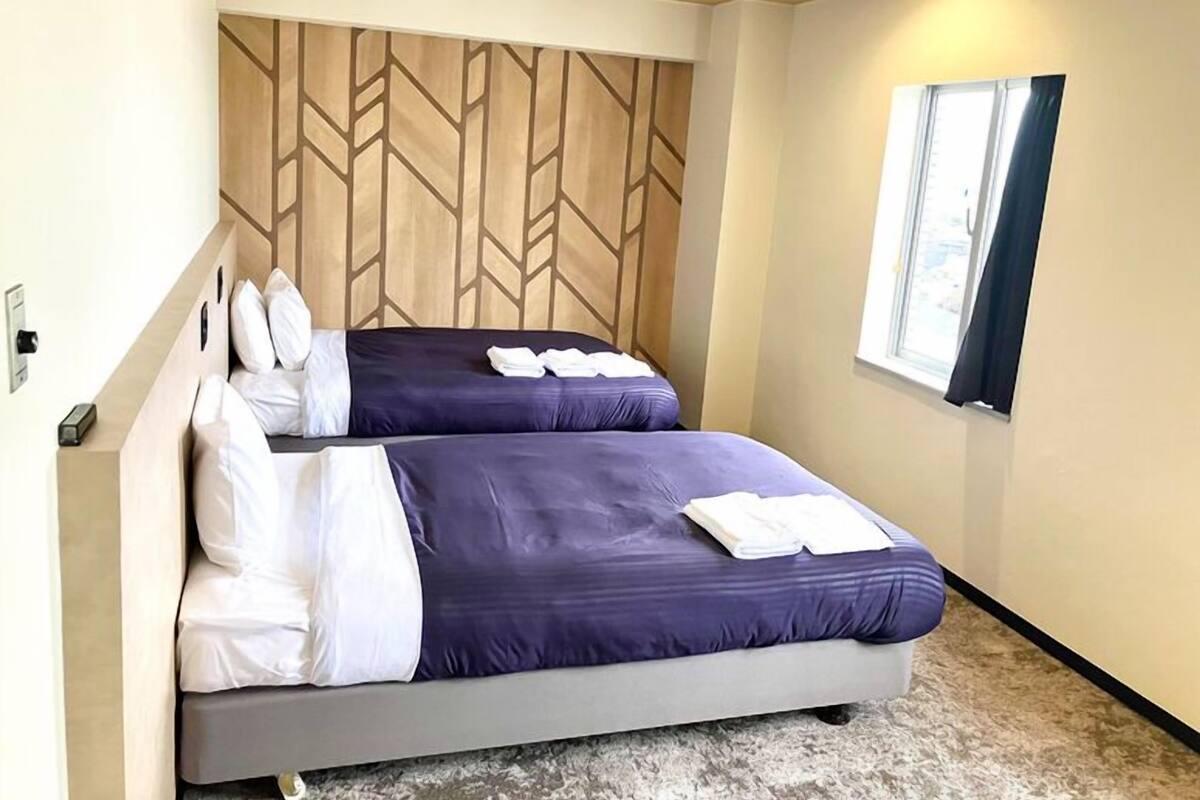 A hotel room with two beds, a wooden headboard, a window, and a carpeted floor.