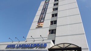 A tall hotel building with a sign reading "HOTEL LIVEMAX" and a large vertical banner advertising hotel services. - HOTEL LiVEMAX Iyo Mishima (Shikokuchuo)