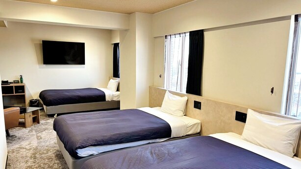 A hotel room with two beds, a flat-screen TV, a desk, and a window with curtains. - HOTEL LiVEMAX Iyo Mishima (Shikokuchuo)