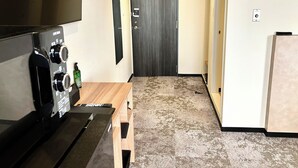 A hallway with a wooden bench, a flat-screen TV mounted on the wall, a door with a sign, and a refrigerator. - HOTEL LiVEMAX Iyo Mishima (Shikokuchuo)