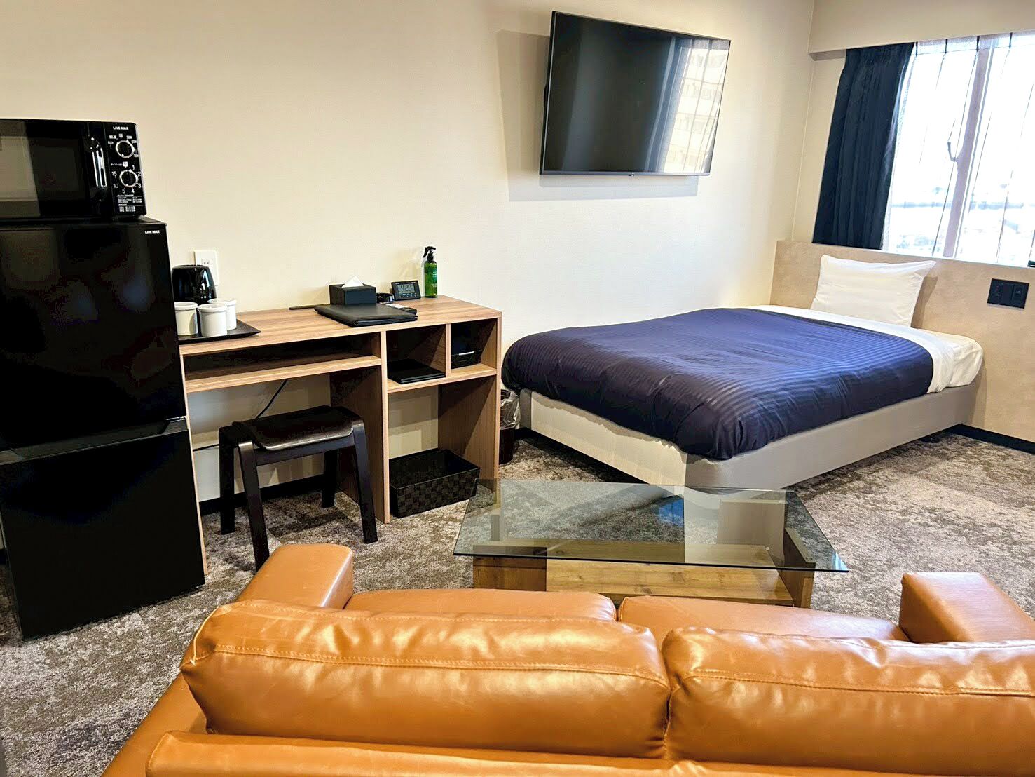 Een hotelkamer met een bed, een bureau, een televisie, een koffiezetapparaat en een leren bank.