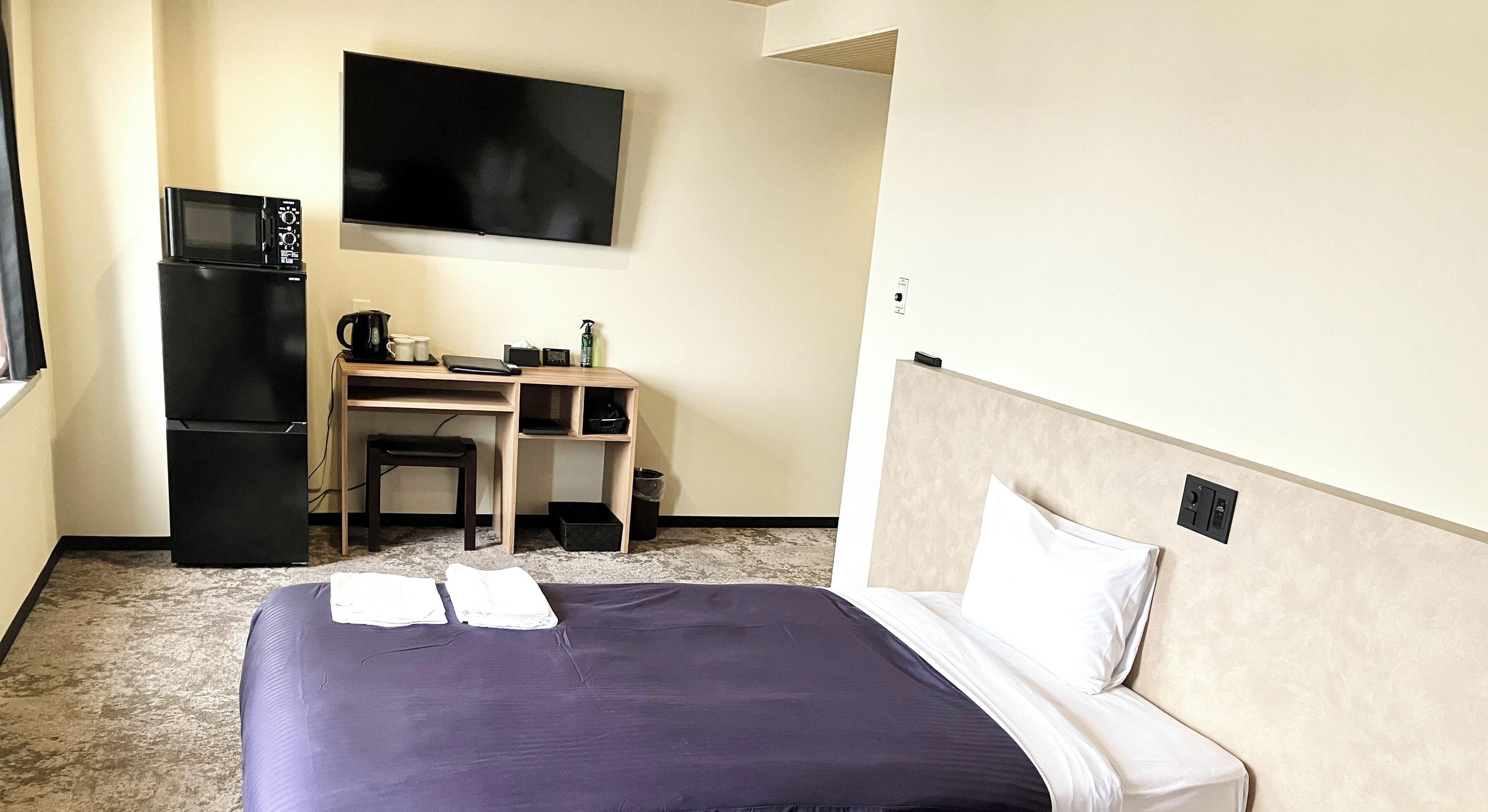 Quarto de hotel com cama, escrivaninha, micro-ondas e televisão.