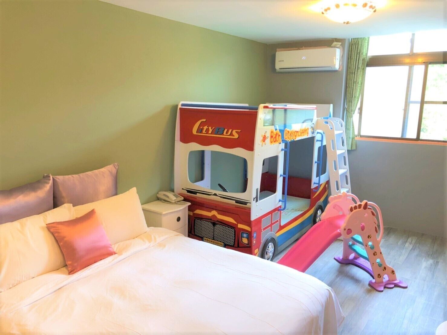 A hotel room with a bed, a toy bus, and a giraffe toy.