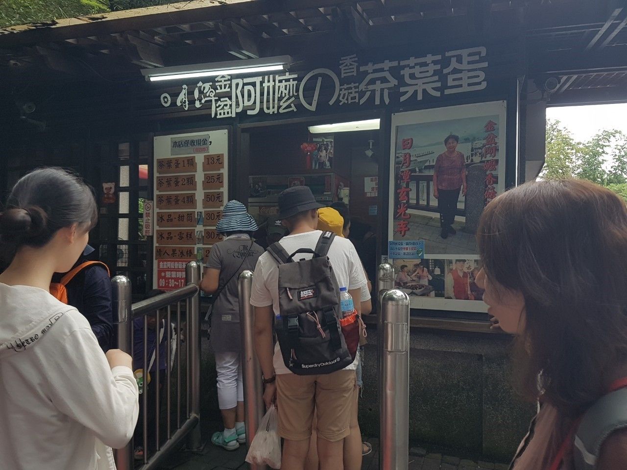 A ticket booth with a sign in a foreign language, a digital display, and a queue of people.