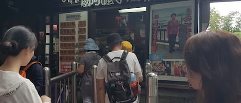 A ticket booth with a sign in a foreign language, a digital display, and a queue of people.