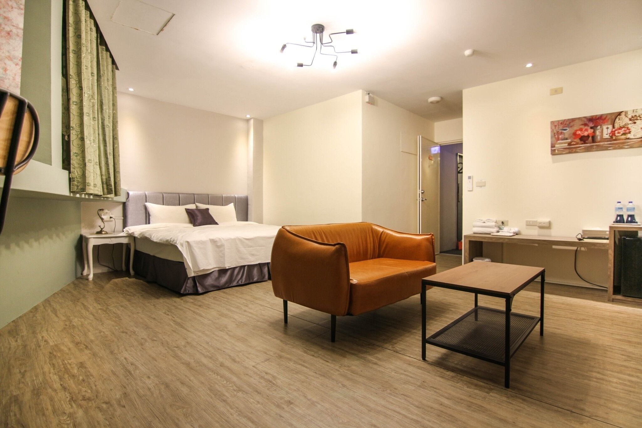 A modern hotel room with a bed, a leather armchair, a small table, and a desk with a computer.