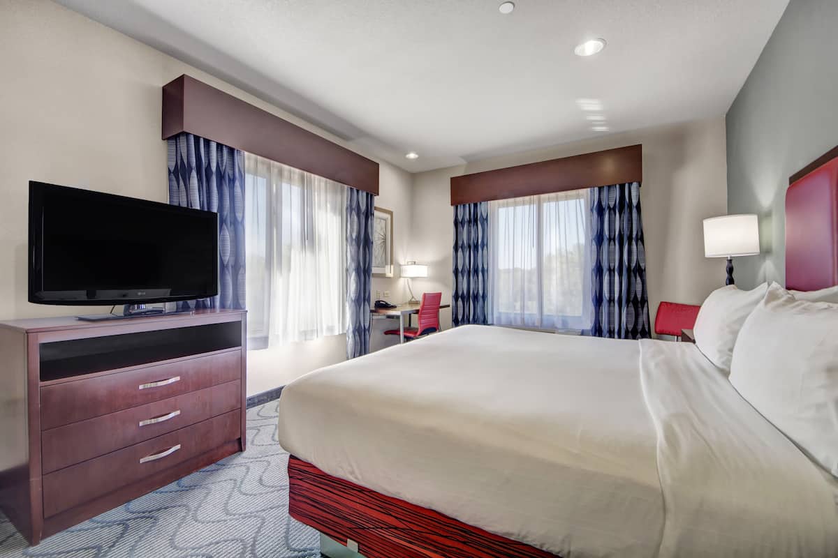 Une chambre d’hôtel avec un grand lit, un téléviseur posé sur une commode en bois et un bureau avec une chaise.