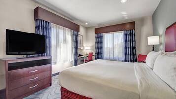 A hotel room with a large bed, a TV on a wooden dresser, and a desk with a chair.