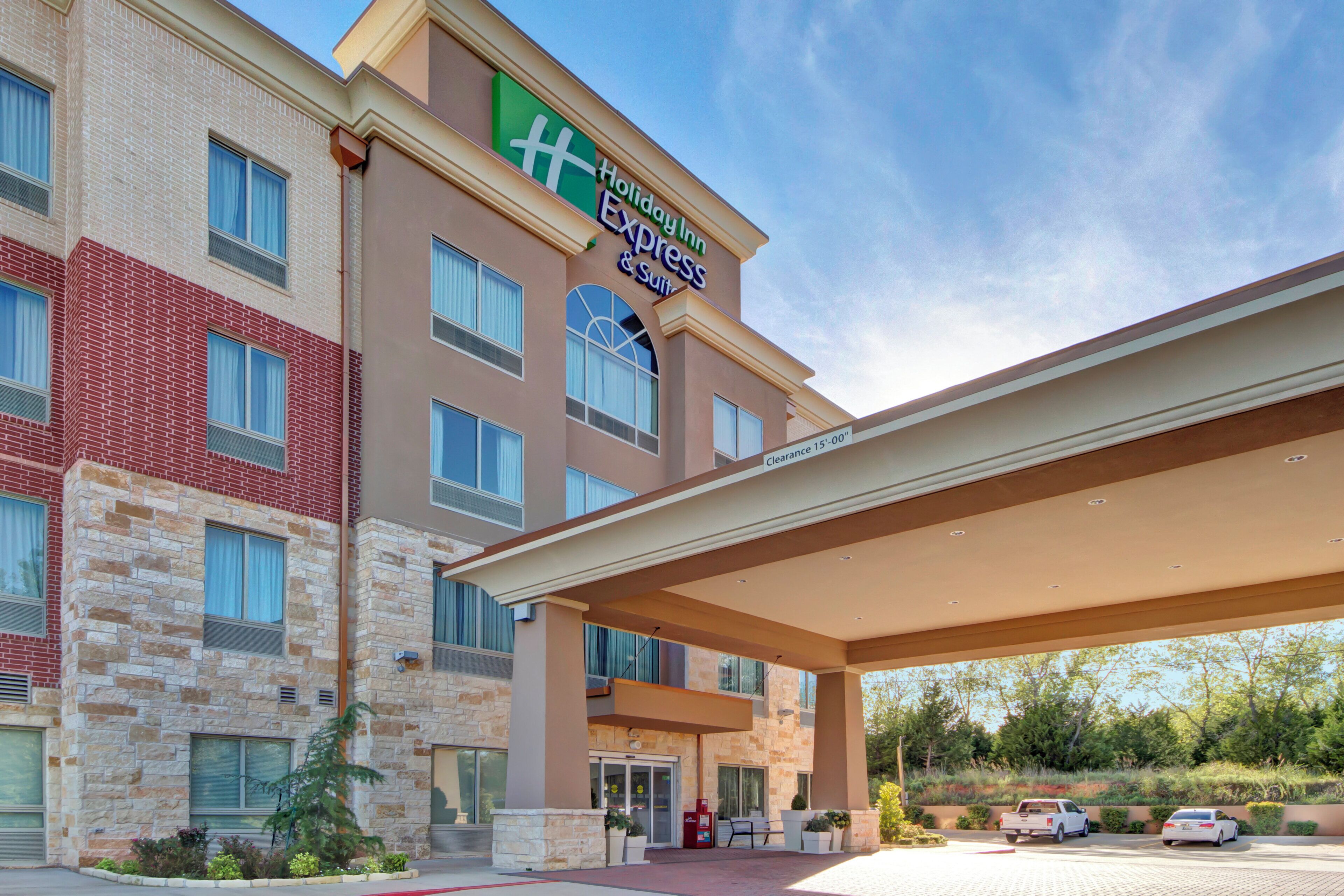 A Holiday Inn Express & Suites building with a brick facade, large windows, and a covered entrance.