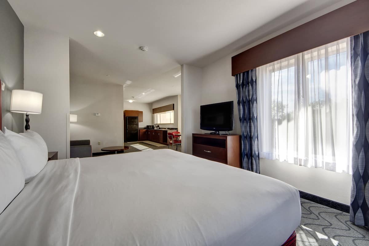 Une chambre d’hôtel avec un grand lit, une télévision, un bureau et une fenêtre avec des rideaux.